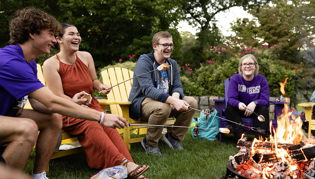 Students roast marshmallows around a fire pit in the fall.