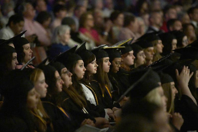 A row of Converse graduates of the Class of 2023 watch the stage during the Commencement ceremony.