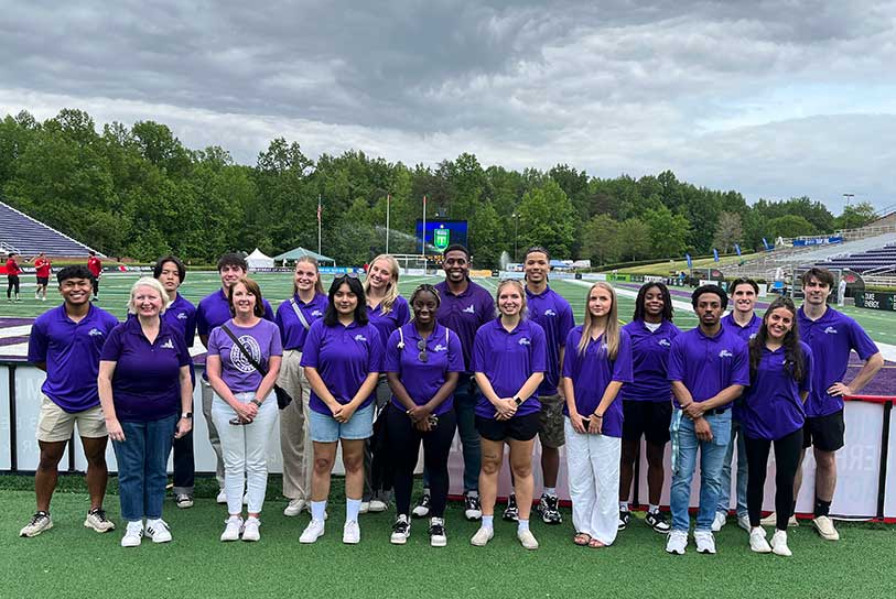 A group of Converse sports management students wearing purple shirts standing on an athletic field.