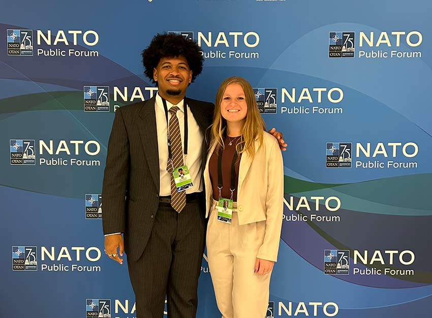 Two Converse Model Programs students stand in front of a NATO backdrop