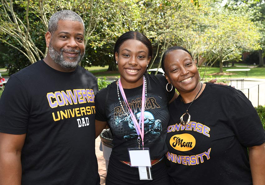 Prospective parents stand next to their child on the Converse campus smiling and wearing Converse University t-shirts.