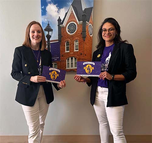 Dean Chandra Hopkins and Jennifer Barksdale ’16 hold up signs to support Rock the Tower in front of a photo of the Wilson Hall tower.