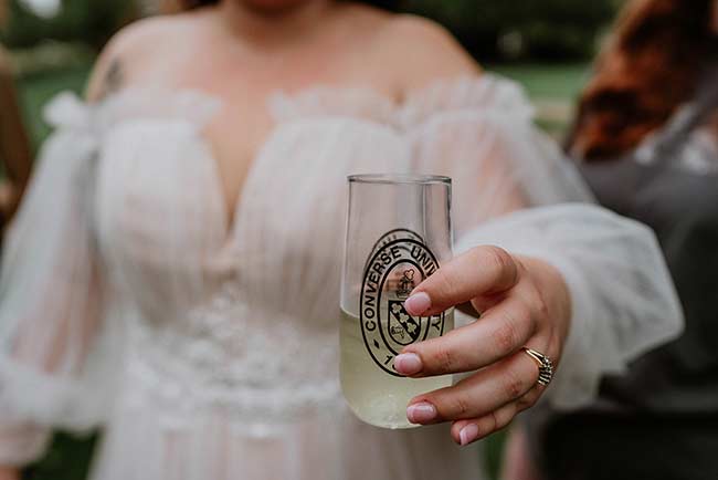 A bride holds a fancy glass with the Converse Unviersity logo on it