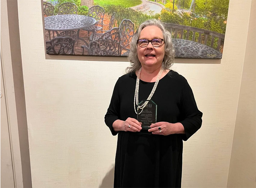 Dr. Gunter smiles while standing in front of artwork holding her award.