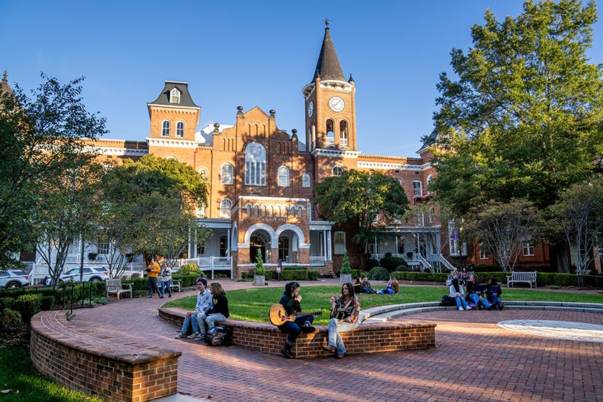 A group of students socialize on the front lawn of Converse campus on a warm, sunny day.