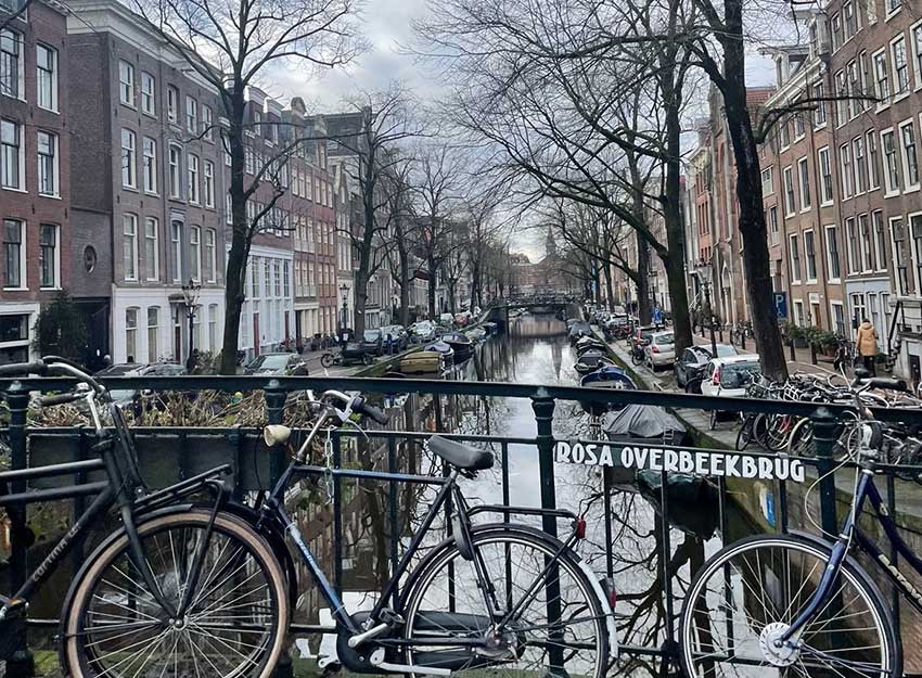 A row of bikes propped on a bridge overlooking a river in Amsterdam on an overcast day.